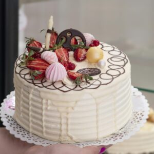Close-up of a beautifully decorated vanilla cream cake topped with fresh strawberries and elegant chocolate details.