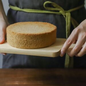 A freshly baked sponge cake being held on a wooden board, ready to serve.
